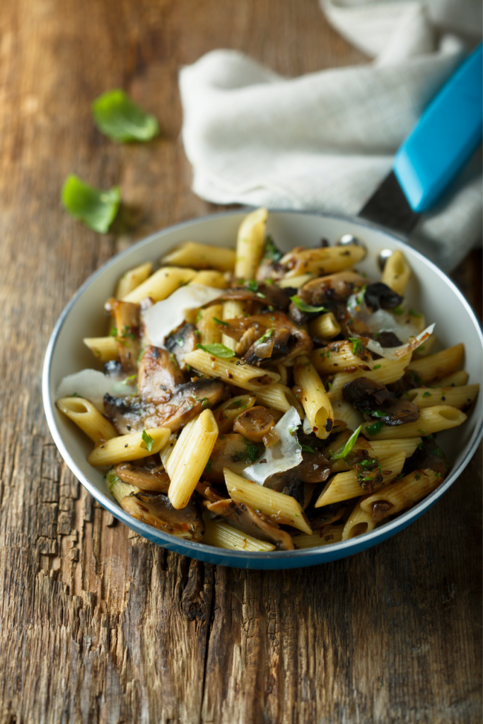 Mushroom pasta in white bowl on natural wooden table- At Your Table
